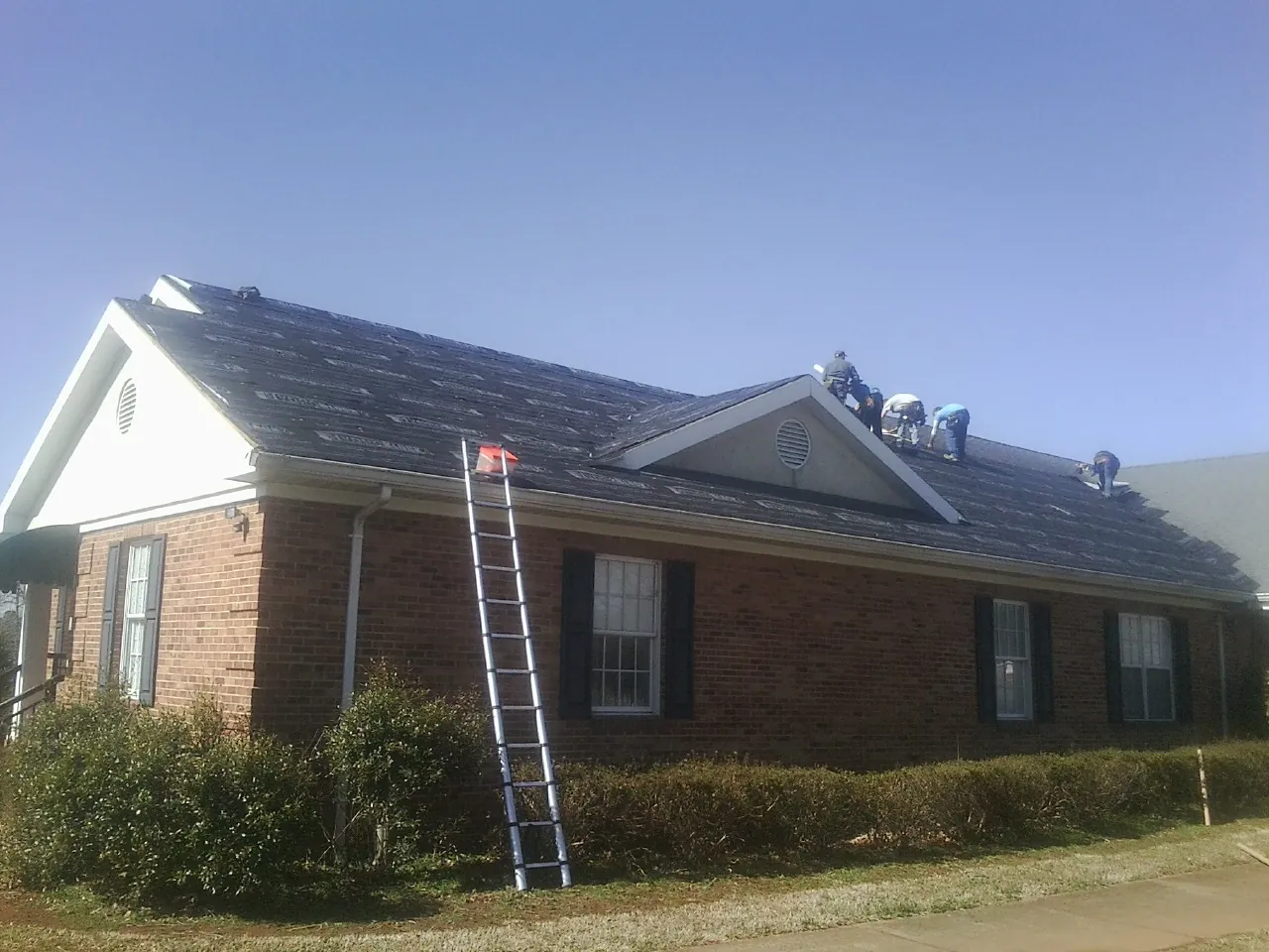 Crew tearing shingles off a brick ranch roof with a ladder set — Emergency Roof Repair work by our crew in Beech Creek