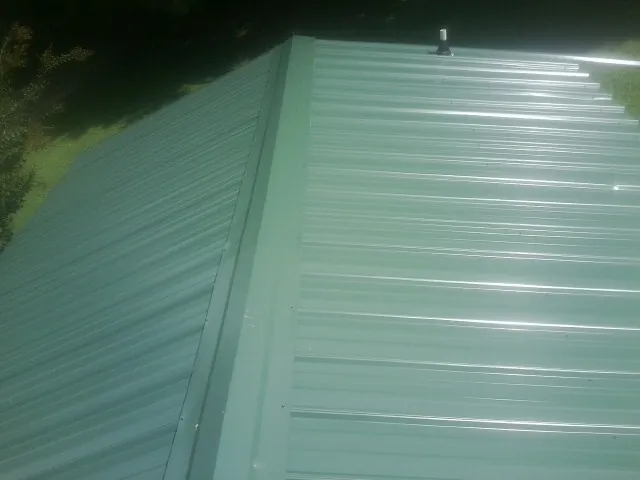 New green metal panels meeting at the ridge of a roof — Flat Roof Repair work by our crew in Beech Creek