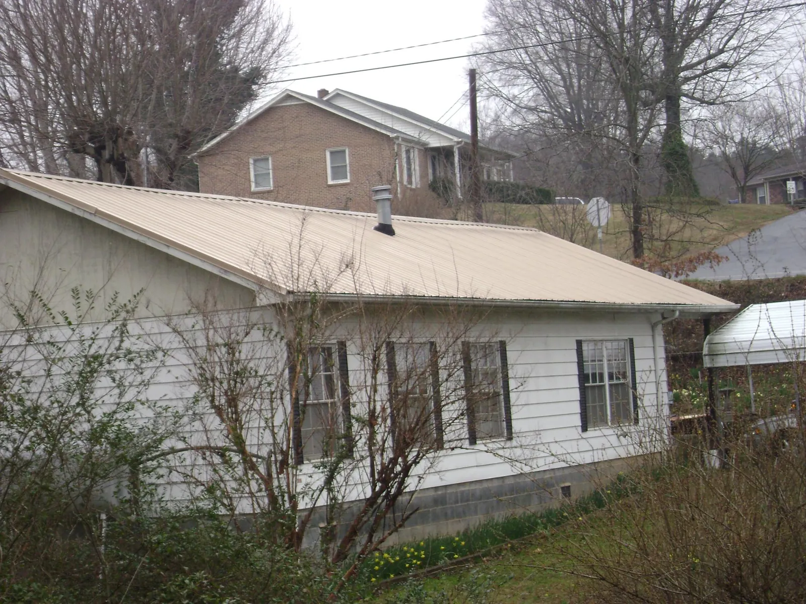 Tan metal roof on a white sided house set into a hillside — Commercial Roofing by Roofing Brothers in Beech Creek